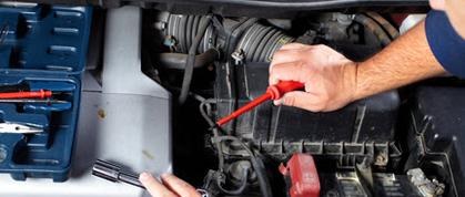 Hands using a red screwdriver and flashlight in an engine bay