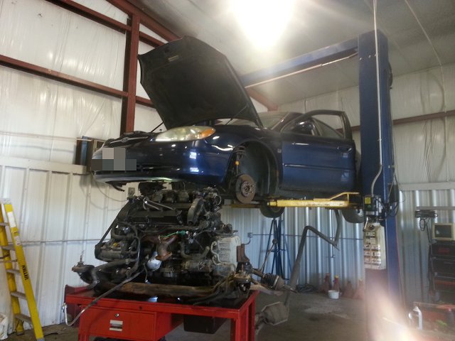 Dark blue sedan raised on a lift with its engine on a stand below