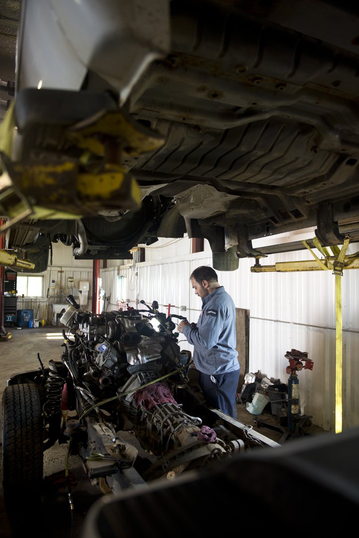 Mechanic in a work uniform working on an engine beneath a vehicle on a lift