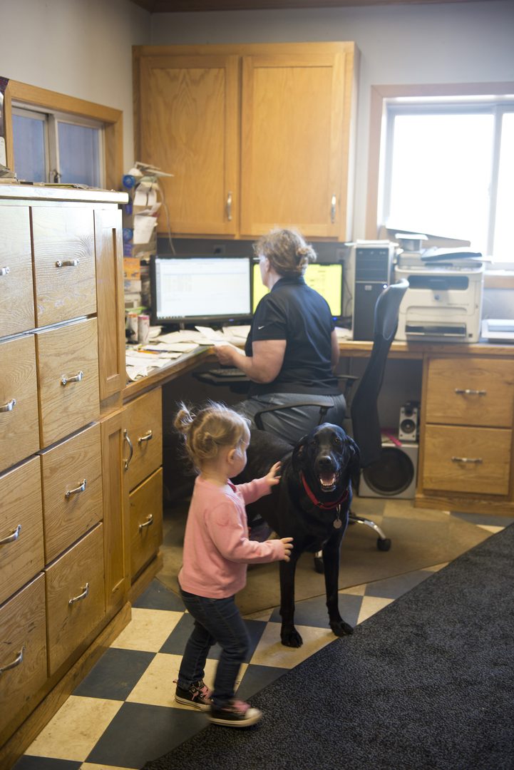 Child petting a black dog in the front office while someone works at a desk